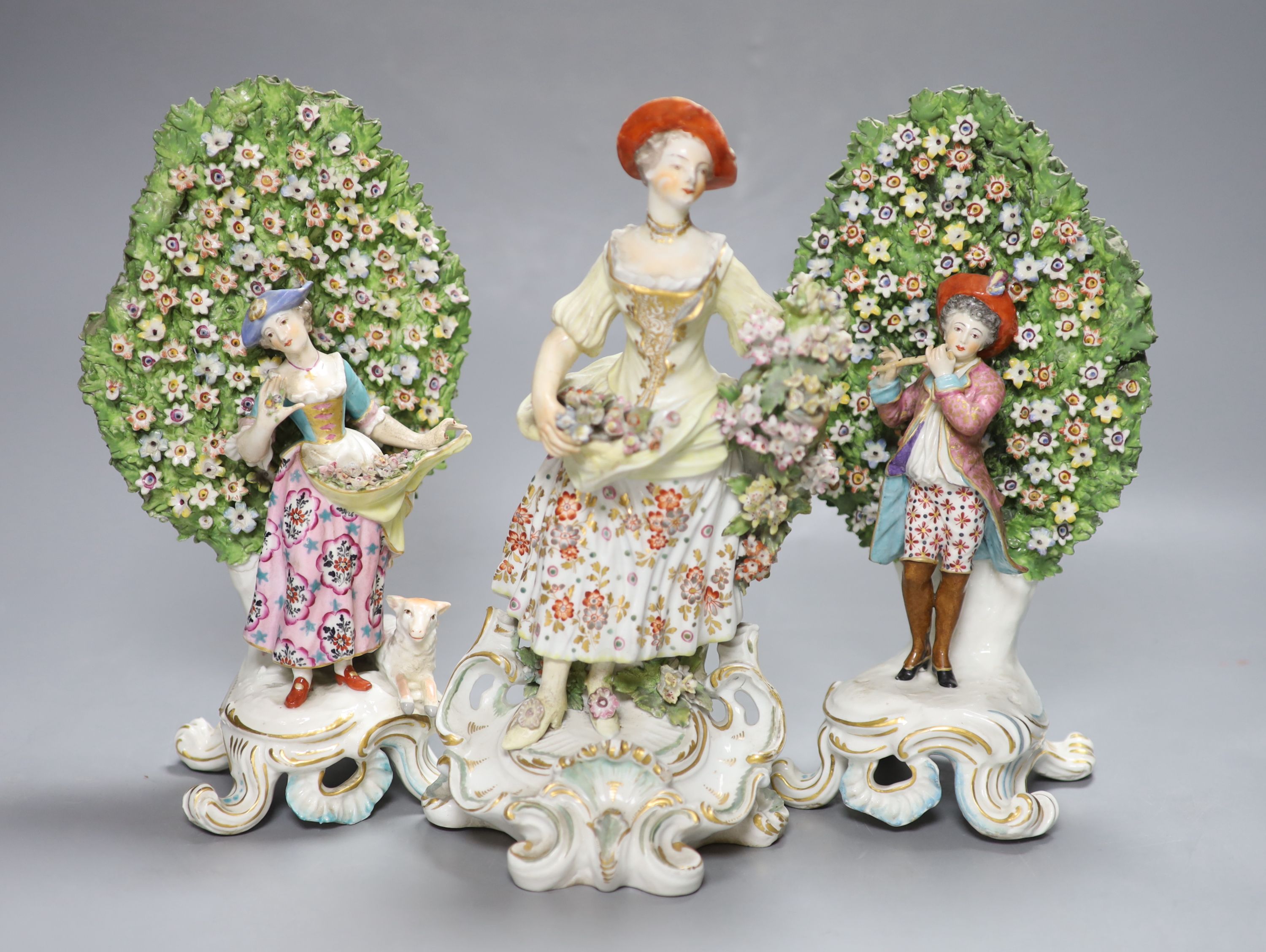 An 18th century Derby figure of a flower seller and a pair of French porcelain bocage groups, tallest 27cm